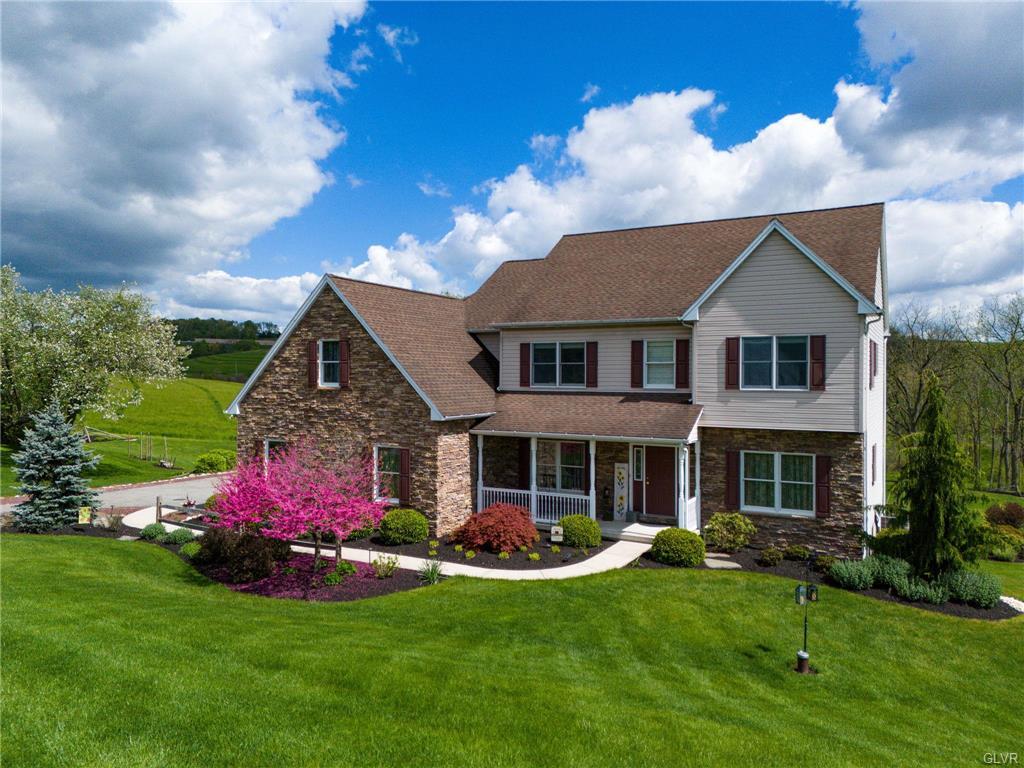 Professional exterior photograph of a two-story home with stonework, a covered porch, and spring landscaping